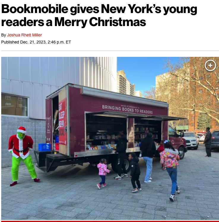 House of SpeakEasy's Bookmobile, parked on a sunny street behind a rack of bikes. A crowd of people is gathered by the Bookmobile's shelves, choosing their books.